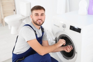 Young plumber fixing washing machine in bathroom